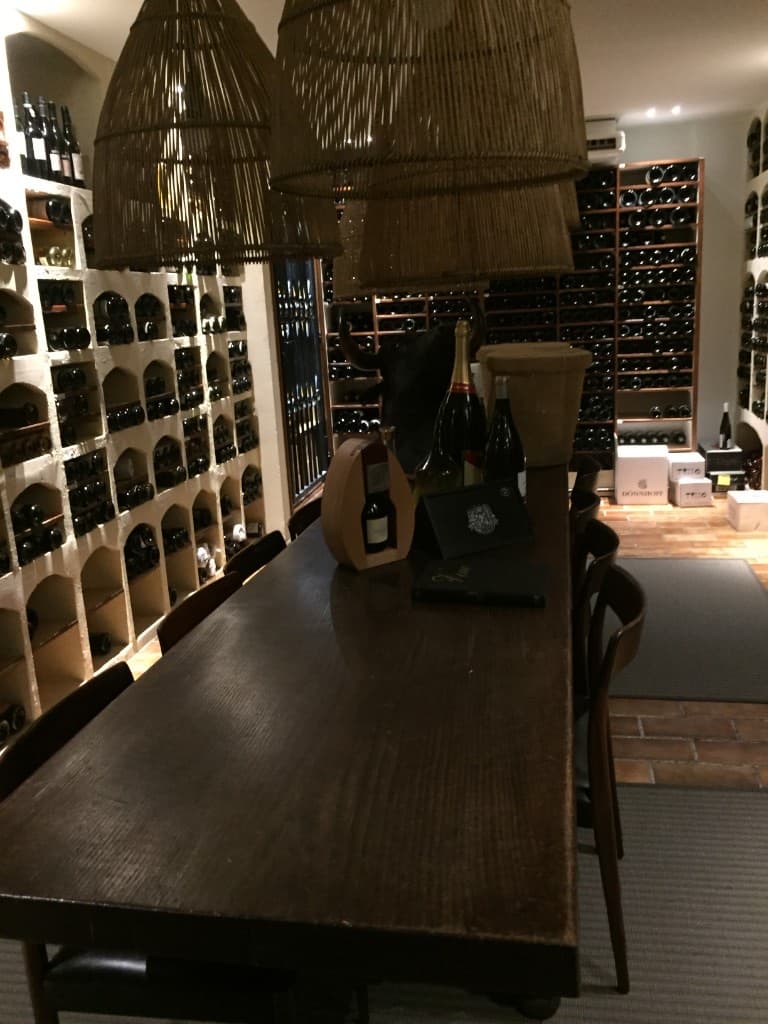 Long cellar table under woven pendant lights with bottles on display